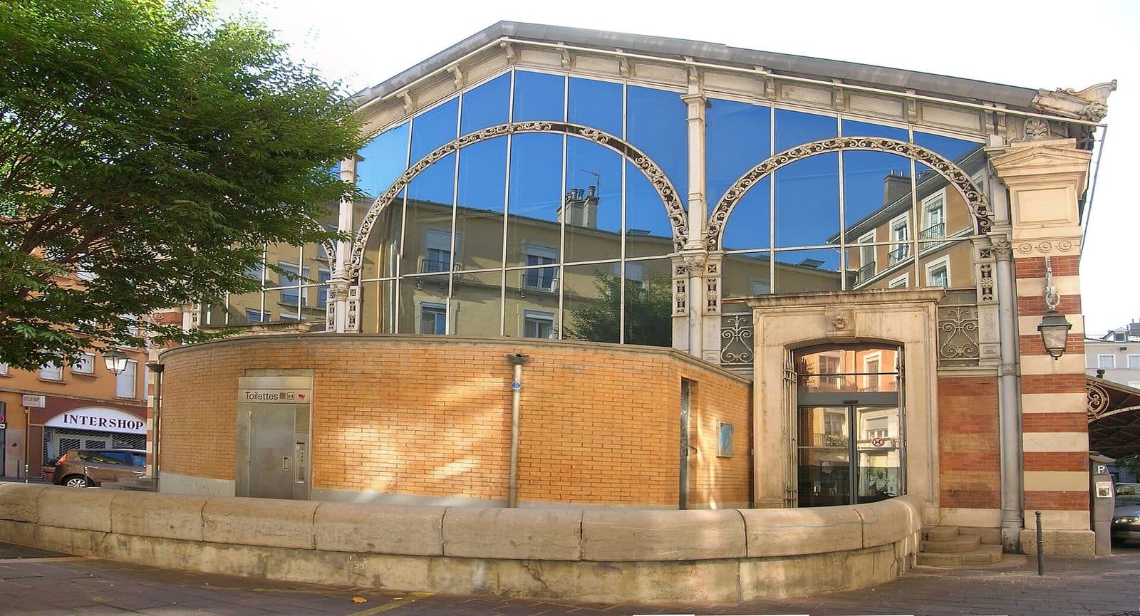 Vue rapprochée de la façade de la halle : grandes verrières cintrées portées par des colonnettes de fonte, sur un soubassement de brique.