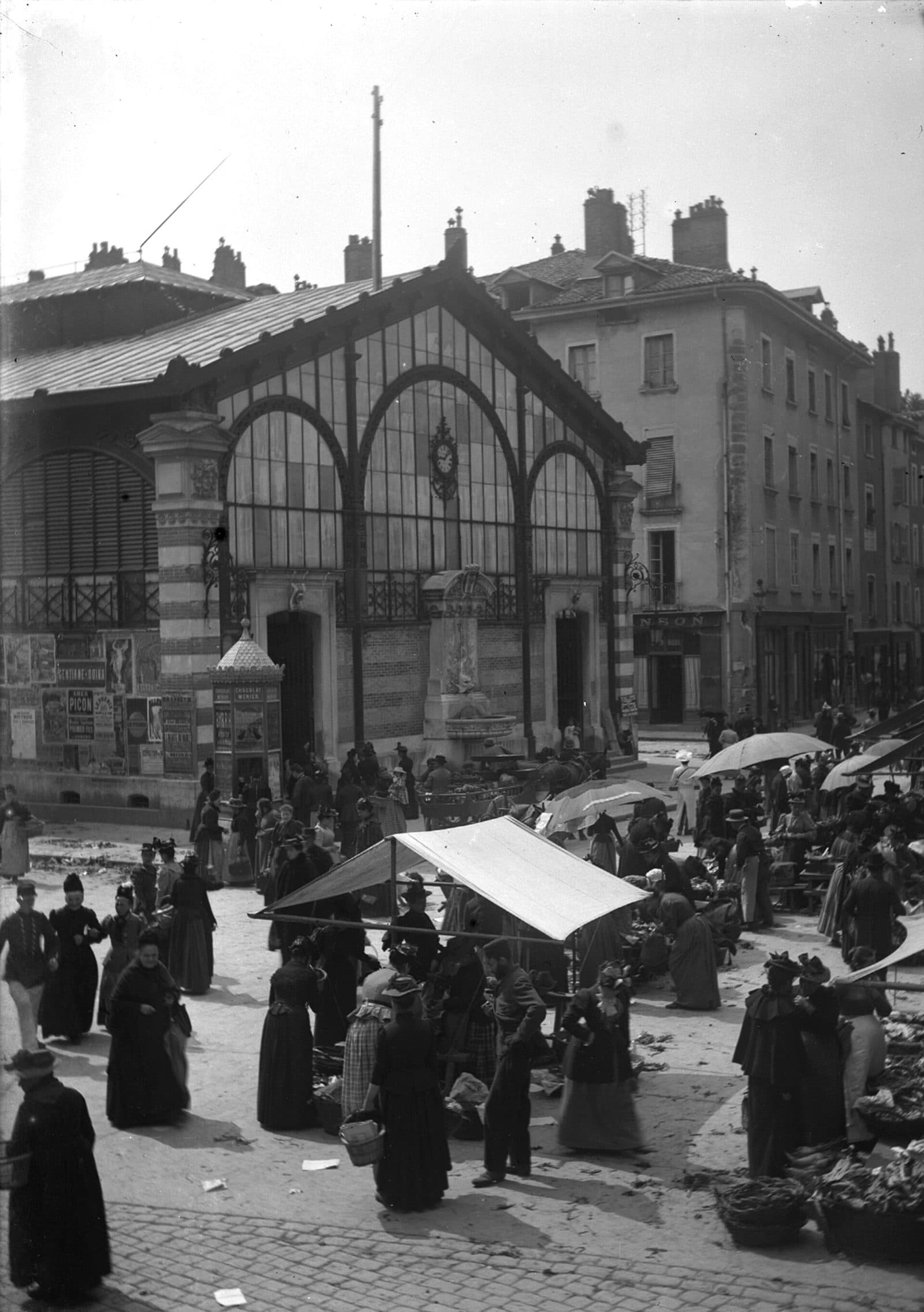 Jour de marché devant la halle Sainte-Claire au début du XXᵉ siècle : la foule, les parasols et les paniers.