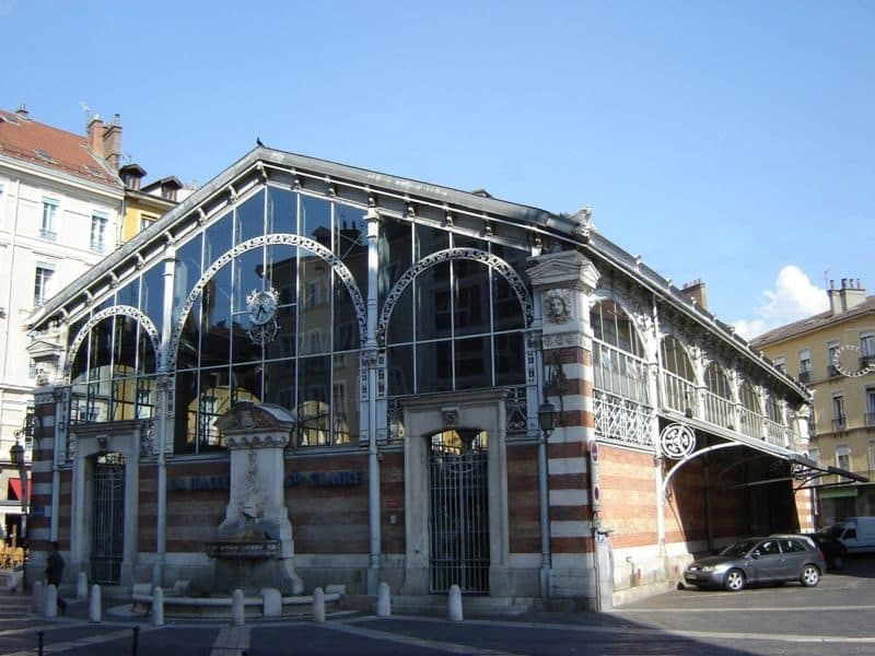 L'angle de la halle Sainte-Claire au soleil, avec la fontaine et la structure de fonte peinte en blanc.