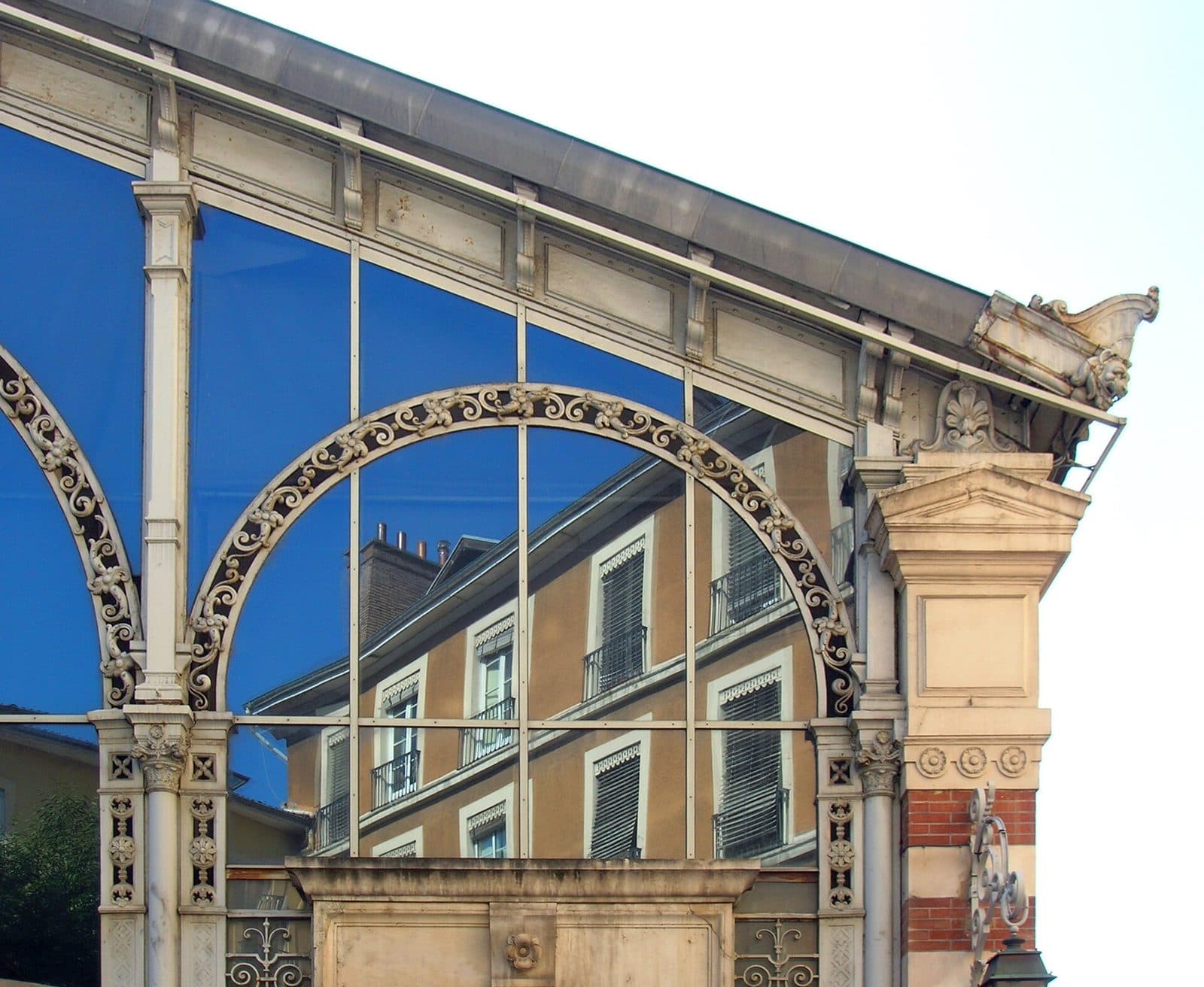 Angle de la halle : la retombée d'un arc de fonte sur son pilier de pierre, surmontée d'un acrotère sculpté.