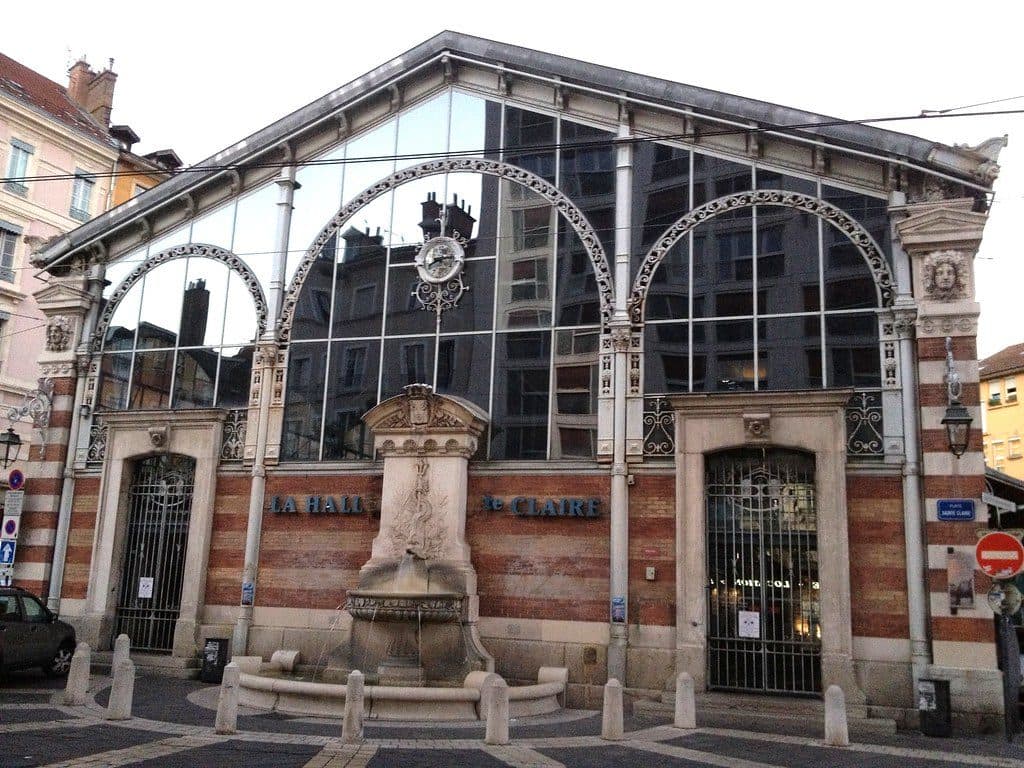 Le pignon de la halle Sainte-Claire portant l'enseigne « La Halle Sainte-Claire », avec son horloge de fer forgé et la fontaine de 1874 au premier plan.