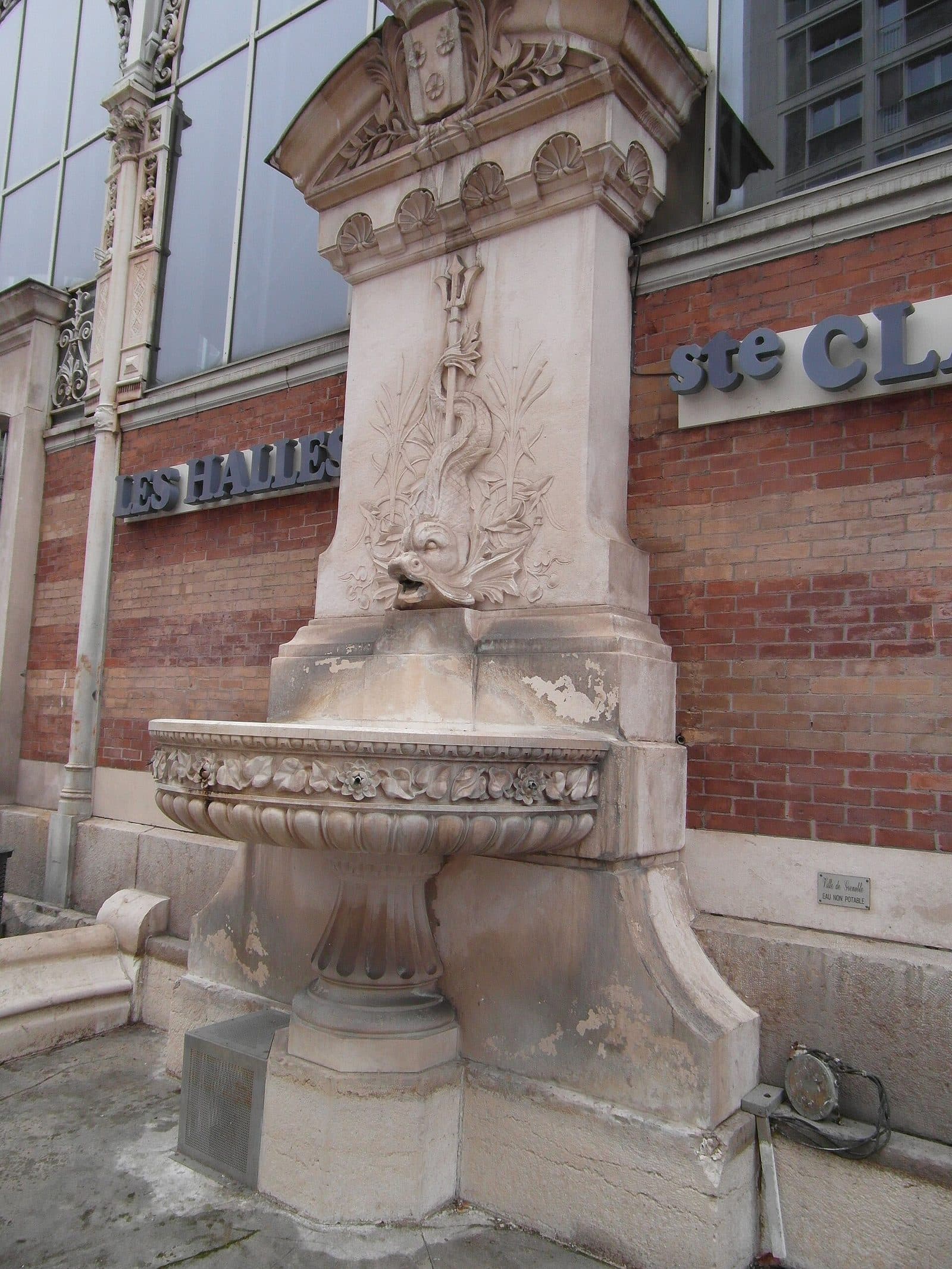 La fontaine de pierre adossée au pignon de la halle, sous l'enseigne « Les Halles Sainte-Claire ».