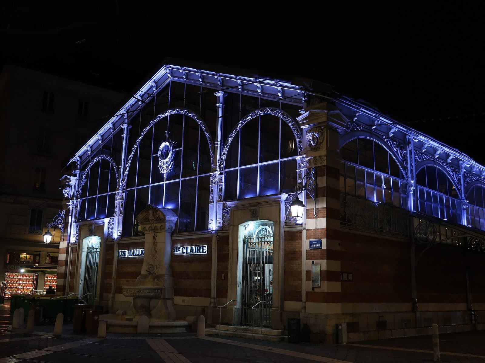 La halle Sainte-Claire de nuit, sa charpente de fonte soulignée par un éclairage bleu.